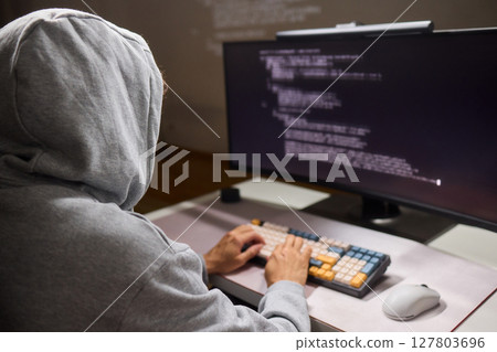 A young programmer codes intently in a dark setting, immersed in his work and creativity 127803696