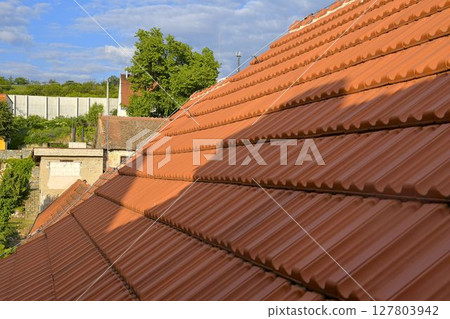 Newly covered roof. New roof covering with red clay tiles. Industrially manufactured tiles on the new roof. Concept of construction, building work, and renovation of the house Newly covered roof. New roof covering with red clay tiles. Industrially manufactured tiles on the new roof. Concept of construction, building work, and renovation of the house 127803942