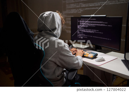 A young programmer codes intently in a dark setting, immersed in his work and creativity 127804022