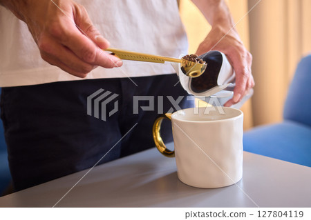Pouring freshly ground coffee beans into a measuring cup for a perfect morning brew 127804119