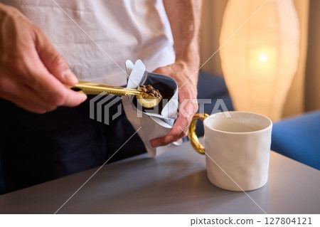 Pouring freshly ground coffee beans into a measuring cup for a perfect morning brew Pouring freshly ground coffee beans into a measuring cup for a perfect morning brew 127804121