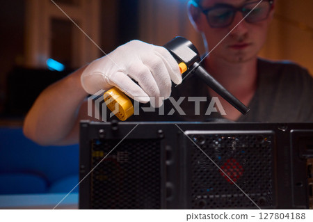 A man cleans a computer case with a vacuum in a bright room, stressing workspace tidiness 127804188