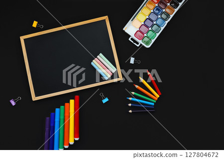 black chalk board and school chalk, felt-tip pens, paints, pen, paper clips, rubber band, on black background top view black chalk board and school chalk, felt-tip pens, paints, pen, paper clips, rubber band, on black background top view 127804672