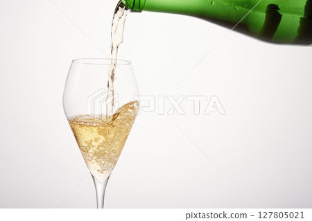 Sparkling wine pours from green bottleneck, creates bubbles. Sparkling wine pours from green bottleneck, creates bubbles. 127805021