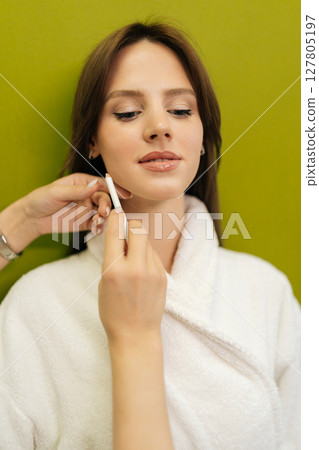 Close-up cropped shot of beautician marking woman face with white pencil, preparing for cosmetic or aesthetic procedure in beauty salon or clinic, standing on isolated green background. Close-up cropped shot of beautician marking woman face with white pencil, preparing for cosmetic or aesthetic procedure in beauty salon or clinic, standing on isolated green background. 127805197