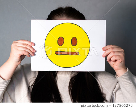 Woman holding emoji mask without smile and any expression in front of face. Social media trends, Gen Z marketing, World emoji day 17 July. Woman holding emoji mask without smile and any expression in front of face. Social media trends, Gen Z marketing, World emoji day 17 July. 127805273