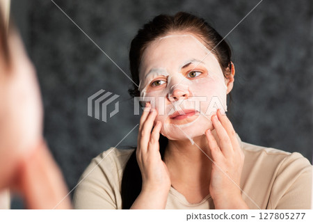 Evening skincare routine. Female applying nourishing face mask. Late night face care. Reflection in bathroom mirror. Dermatology concept. Evening skincare routine. Female applying nourishing face mask. Late night face care. Reflection in bathroom mirror. Dermatology concept. 127805277