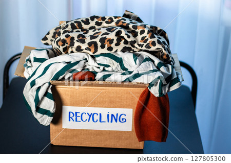 Woman prepared cardboard box full of used outfits for recycling. Responsible disposal and secondhand fashion concept. Woman prepared cardboard box full of used outfits for recycling. Responsible disposal and secondhand fashion concept. 127805300