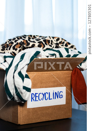Cardboard box full of clothes labeled Recycling. Concept of sustainable fashion and responsible wardrobe management. Cardboard box full of clothes labeled Recycling. Concept of sustainable fashion and responsible wardrobe management. 127805301