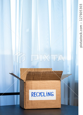 Woman prepared cardboard box full of used outfits for recycling. Responsible disposal and secondhand fashion concept. 127805303