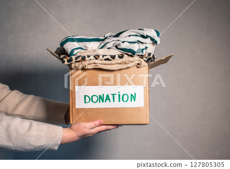 Woman folding clothes and placing them into donation box. Concept of charity and wardrobe decluttering. 127805305