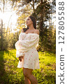 Young woman in a light summer dress standing in a sunny forest clearing 127805588