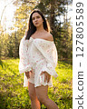 Young woman in a light summer dress standing in a sunny forest clearing 127805589