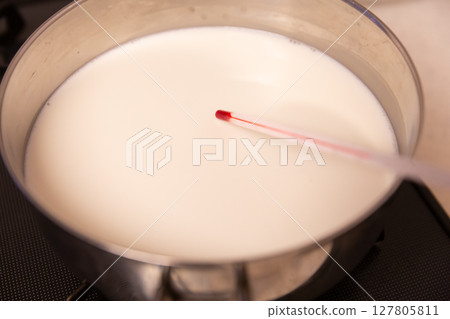 Heating milk in a pot and a thermometer 127805811
