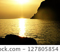 Stunning golden sunset over the sea in Calabria, Italy, with soft sunlight reflecting on the water and the curved silhouette of mountain cliffs in the distance. Serene coastal landscape with warm 127805854