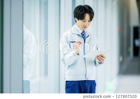 一名身穿工作服的男子在辦公室走廊操作平板電腦 127807320