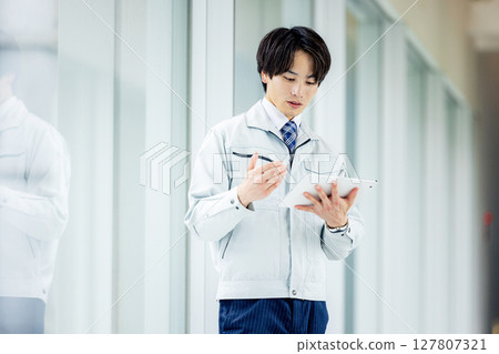 一名身穿工作服的男子在辦公室走廊操作平板電腦 127807321