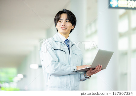 辦公室走廊裡穿著工作服、帶著筆記型電腦的年輕工人 辦公室走廊裡穿著工作服、帶著筆記型電腦的年輕工人 127807324