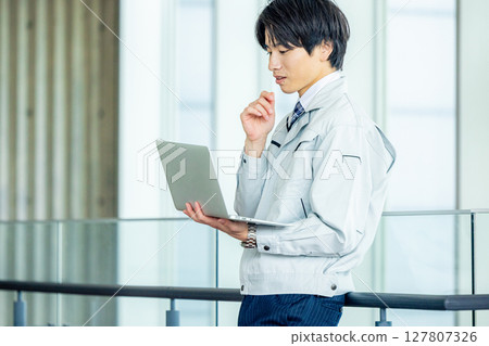 辦公室走廊裡穿著工作服、帶著筆記型電腦的年輕工人 127807326