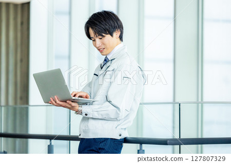 辦公室走廊裡穿著工作服、帶著筆記型電腦的年輕工人 127807329