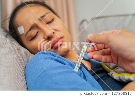 A woman carefully monitoring her fever while she is resting comfortably at home A woman carefully monitoring her fever while she is resting comfortably at home 127808513
