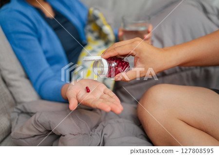 Caring Gesture Giving Medication with Water on a Cozy Couch, Creating Comfort 127808595
