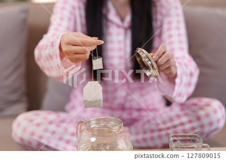 Asian adult woman hands preparing hot herbal tea bags for relaxing mindful morning ritual at home 127809015