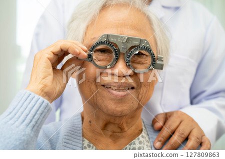 Optometrist checking Asian elderly woman ophthalmic vision eye test and using optical trial frame. 127809863