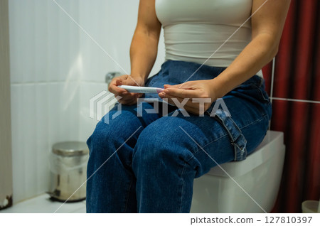 A woman takes an express pregnancy test while sitting on the toilet. 127810397