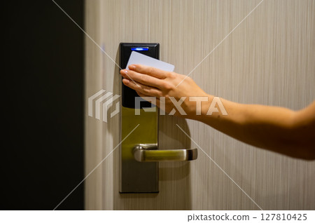 A woman opens an electronic lock with a card and enters a hotel room.  127810425