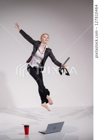 Barefoot ballerina in business suit jumping with laptop on white background.  127810464
