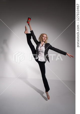 Barefoot ballerina in business suit dancing with a cup of coffee on a white background. Barefoot ballerina in business suit dancing with a cup of coffee on a white background. 127810467