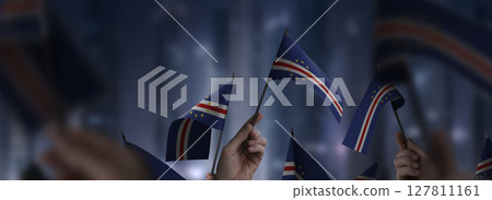 Cape Verde flags in their hands on a blurred urban background Cape Verde flags in their hands on a blurred urban background 127811161