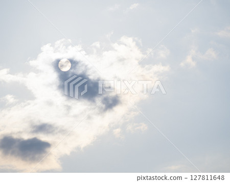 The sun is hidden by clouds and only its outline is visible (bright) 127811648