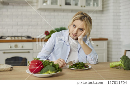 Sad bored woman keeping to diet, doesnt want to eat vegetable salad, dreaming about something tasty 127811704