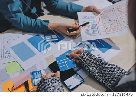 Group of young application developers analyzing uxui mobile app templates during a working meeting Group of young application developers analyzing uxui mobile app templates during a working meeting 127815476