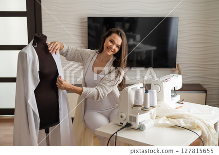 Caucasian woman sews a dress at home. Workspace of a seamstress Caucasian woman sews a dress at home. Workspace of a seamstress 127815655