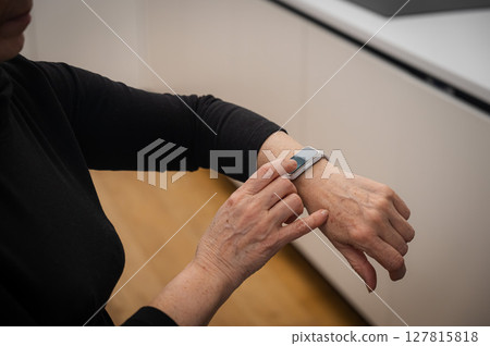 Elderly Caucasian woman looking at smart watch. Close-up of hands. Elderly Caucasian woman looking at smart watch. Close-up of hands. 127815818