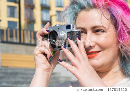 Caucasian woman with curly colored hair takes pictures on an old retro camera outdoors Caucasian woman with curly colored hair takes pictures on an old retro camera outdoors 127815820