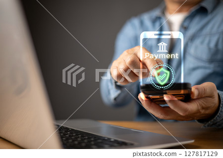 A man uses a laptop while interacting with a futuristic digital payment interface. The holographic screen displays a secure online payment symbol, highlighting financial technology advancements. A man uses a laptop while interacting with a futuristic digital payment interface. The holographic screen displays a secure online payment symbol, highlighting financial technology advancements. 127817129