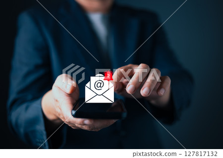 businessman in suit interacts with a digital email notification icon hovering above his smartphone. The glowing envelope with symbol and a red alert signifies mail, inbox updates, and communication. businessman in suit interacts with a digital email notification icon hovering above his smartphone. The glowing envelope with symbol and a red alert signifies mail, inbox updates, and communication. 127817132