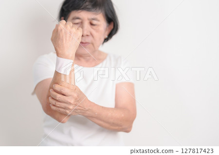 Elderly Woman having wrist pain with Medicated pain relief patch plaster for Carpal Tunnel Syndrome, Wrist Tendinitis, muscle ache, De Quervain s tenosynovitis, Hand Osteoarthritis and Senior health 127817423