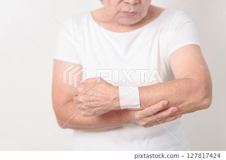 Elderly Woman having wrist pain with Medicated pain relief patch plaster for Carpal Tunnel Syndrome, Wrist Tendinitis, muscle ache, De Quervain s tenosynovitis, Hand Osteoarthritis and Senior health 127817424