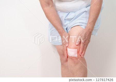 Elderly woman having knee ache with Medicated pain relief patch plaster to Runners Knee or Patellofemoral Pain Syndrome, osteoarthritis, arthritis, rheumatism and Patellar Tendinitis. Senior health 127817426
