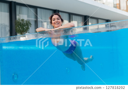 Happy caucasian woman swims in an outdoor pool with a transparent wall in a hotel 127818202
