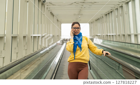 Happy woman stands on a travelator and talks on a cell phone 127818227