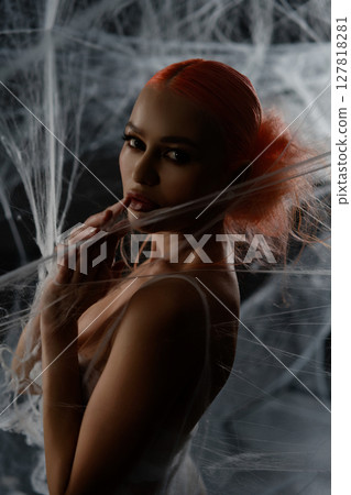 Red-haired woman entangled in a delicate net trap in an artistic display 127818281