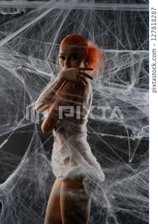 Woman trapped in a web of silky strands, showcasing her striking red hair Woman trapped in a web of silky strands, showcasing her striking red hair 127818287