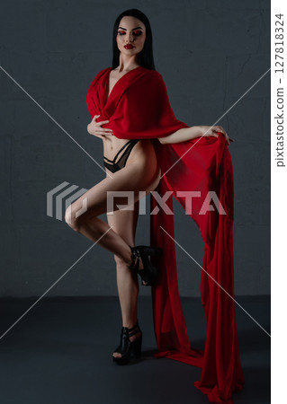 Elegant woman posing in red lingerie with flowing fabric draped on her shoulders 127818324