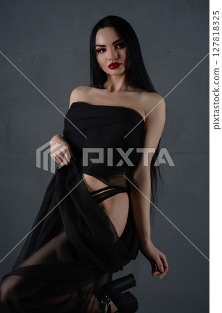 Elegant woman showcases lingerie with a flowing fabric against a gray backdrop 127818325